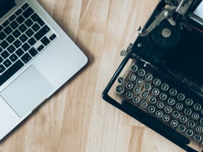 A laptop and a typewriter on a wooden desk, reflecting the differences for sage intacct versus sage 100