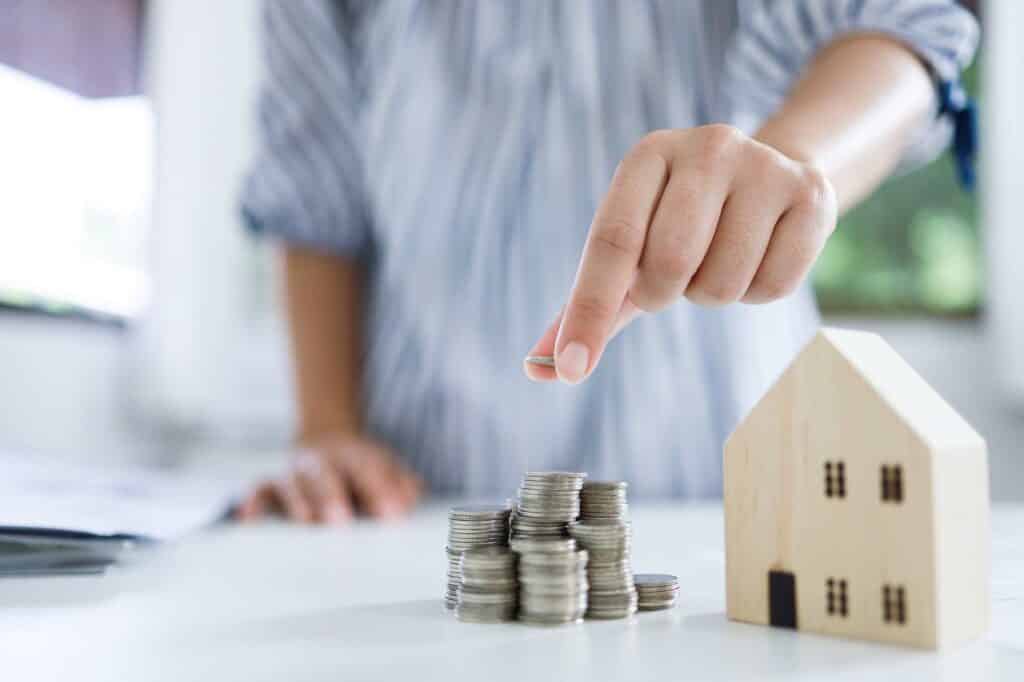 A woman is pointing to a pile of coins and a house model.