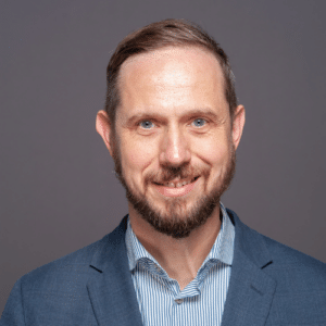 A man with a beard and striped shirt is smiling.