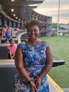 A woman in a blue dress standing in front of a baseball field.