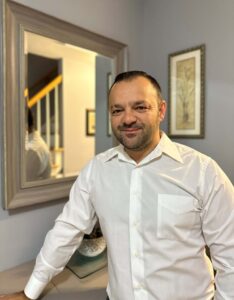 A man in a white shirt standing in front of a mirror.