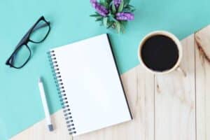 A notebook, a cup of coffee and a pen on a wooden table.