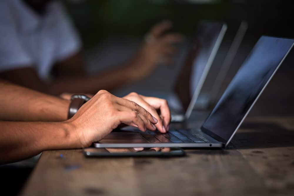 A man is typing on a laptop on a wooden table.