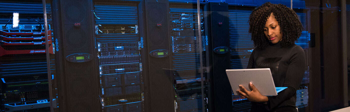 A woman in a server room holding a tablet.