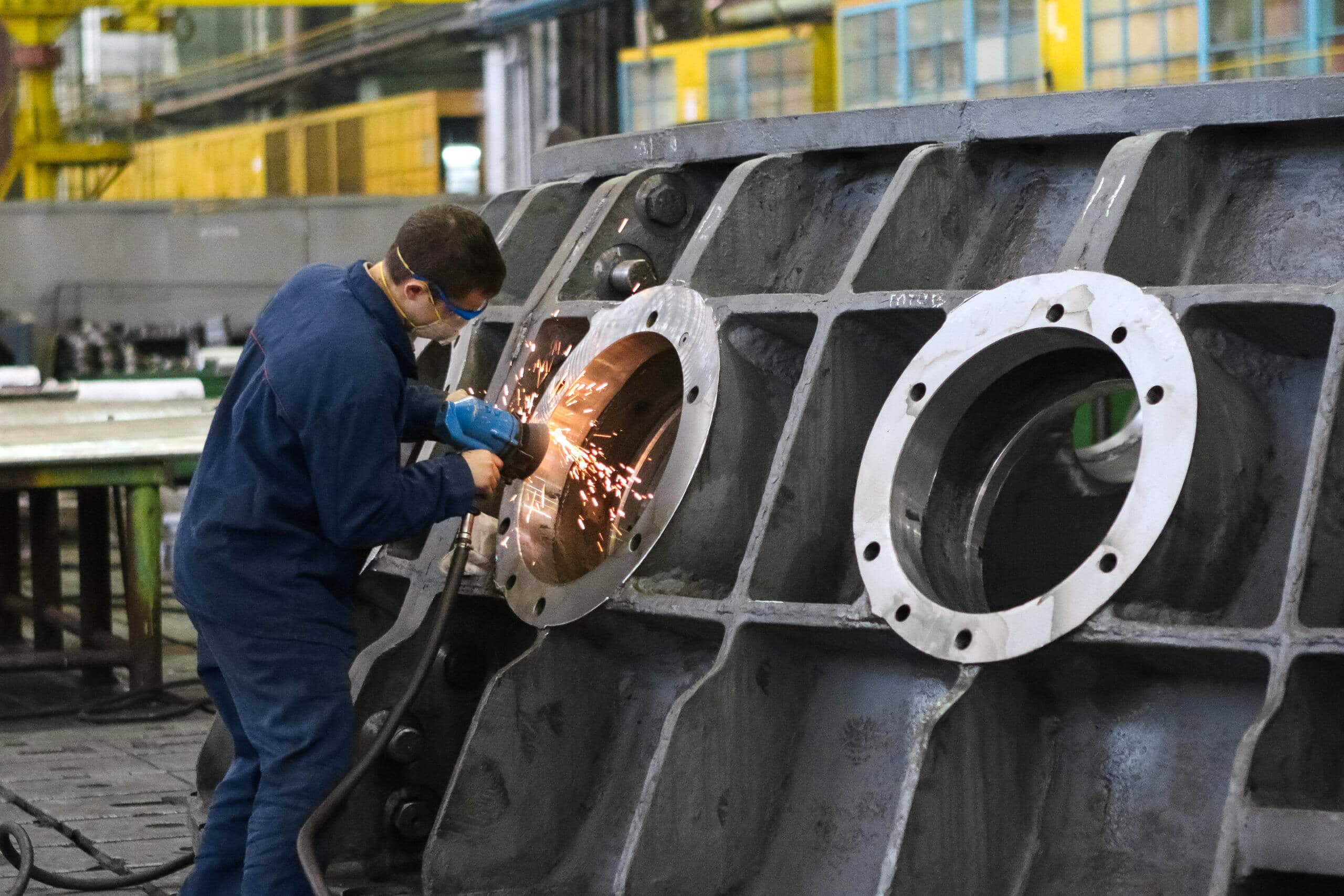 A worker is welding a large metal piece in a factory.