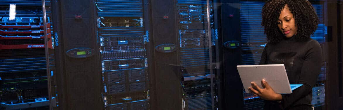 A woman in a server room holding a laptop.