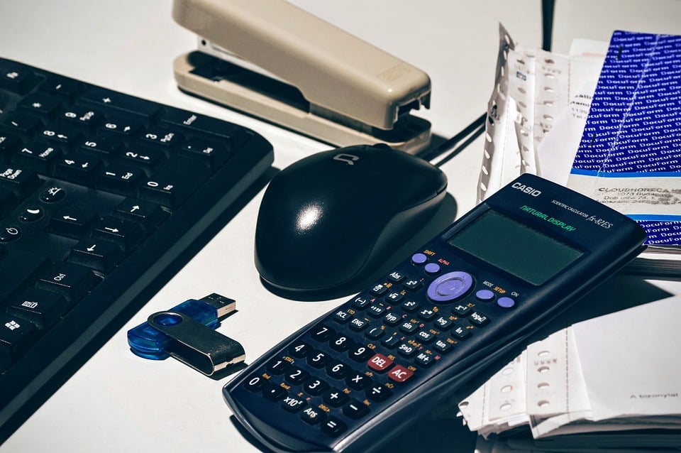 A calculator on a desk next to a mouse and keyboard.
