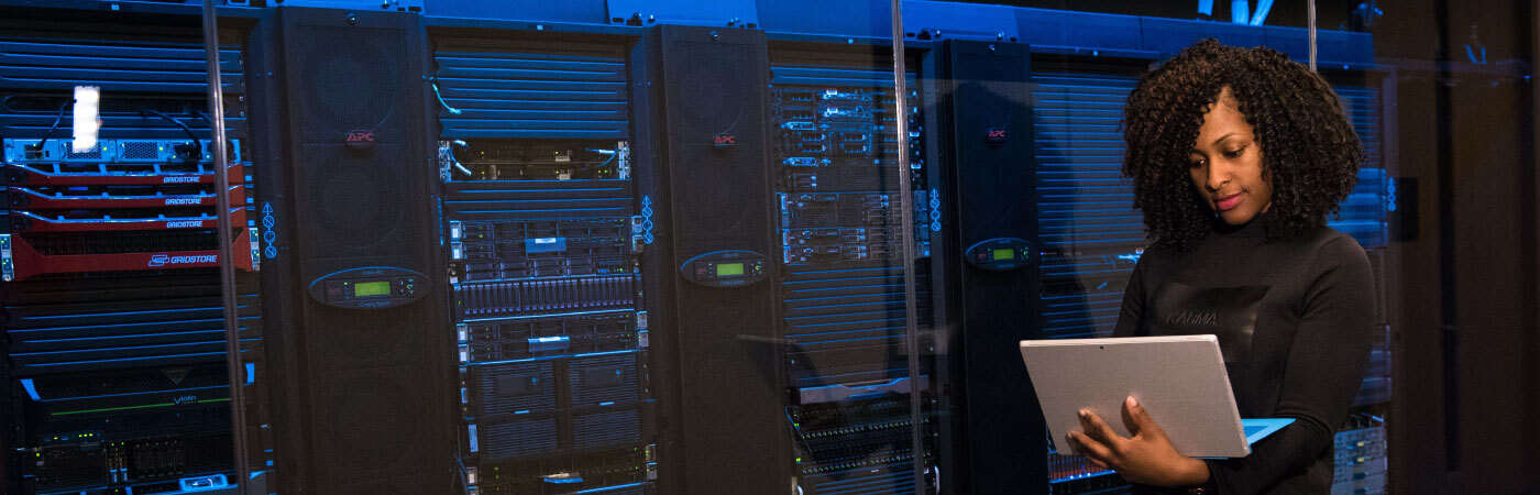 A woman in a server room holding a tablet.