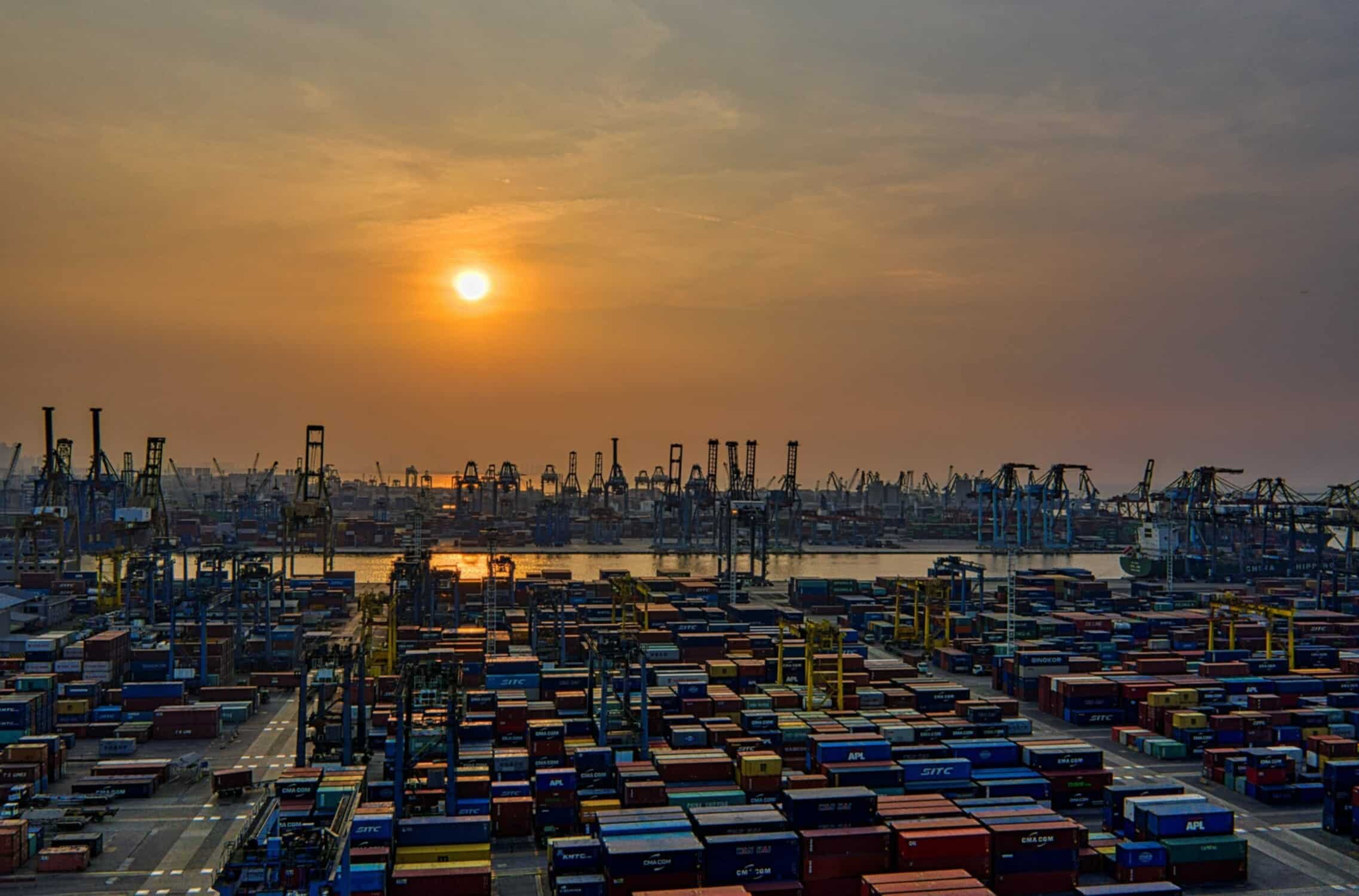 The sun is setting over a dock full of containers.