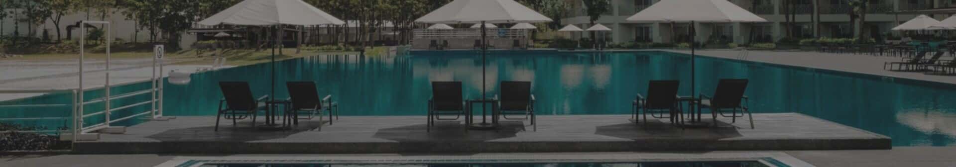 A swimming pool with chairs and umbrellas next to it.