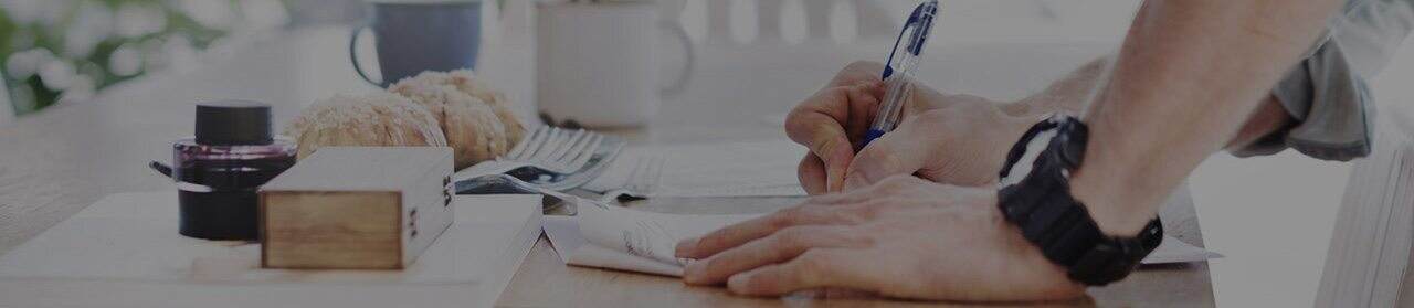 A man writing on a desk with a pen.