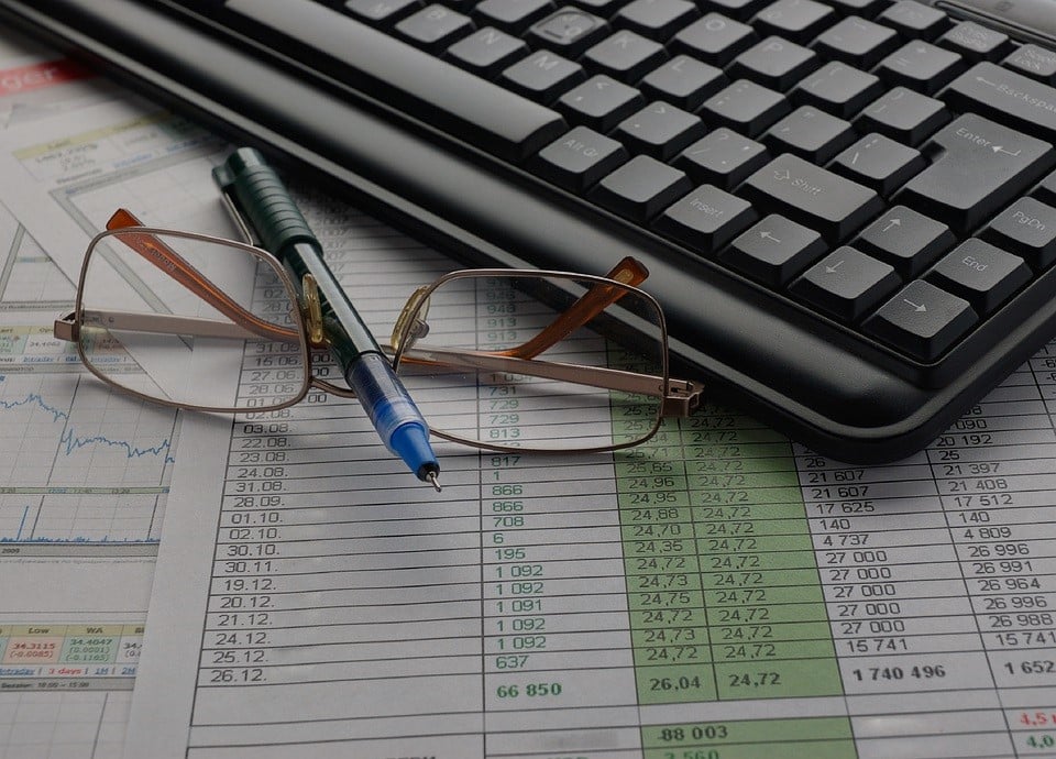 A pen, glasses, and a keyboard on a desk.