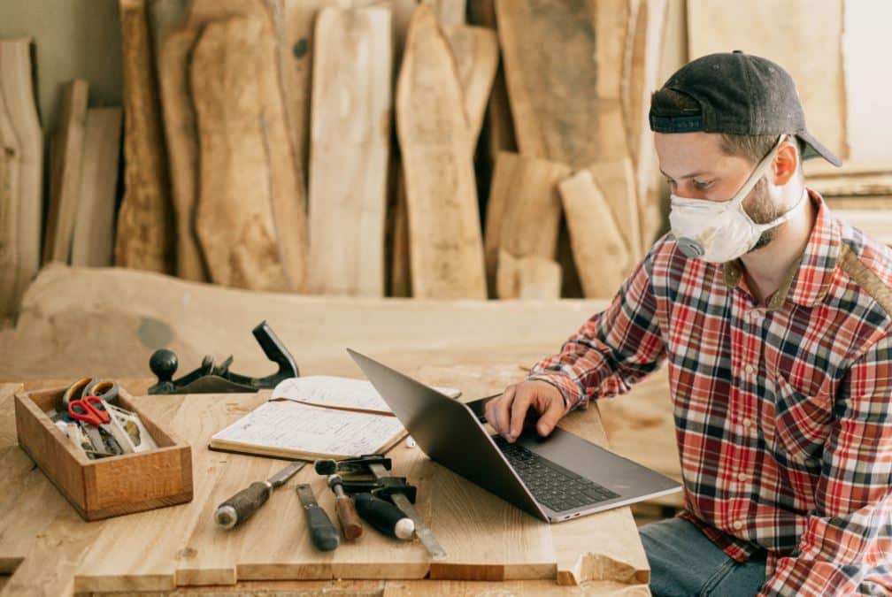 A man wearing a face mask working on a wooden table.