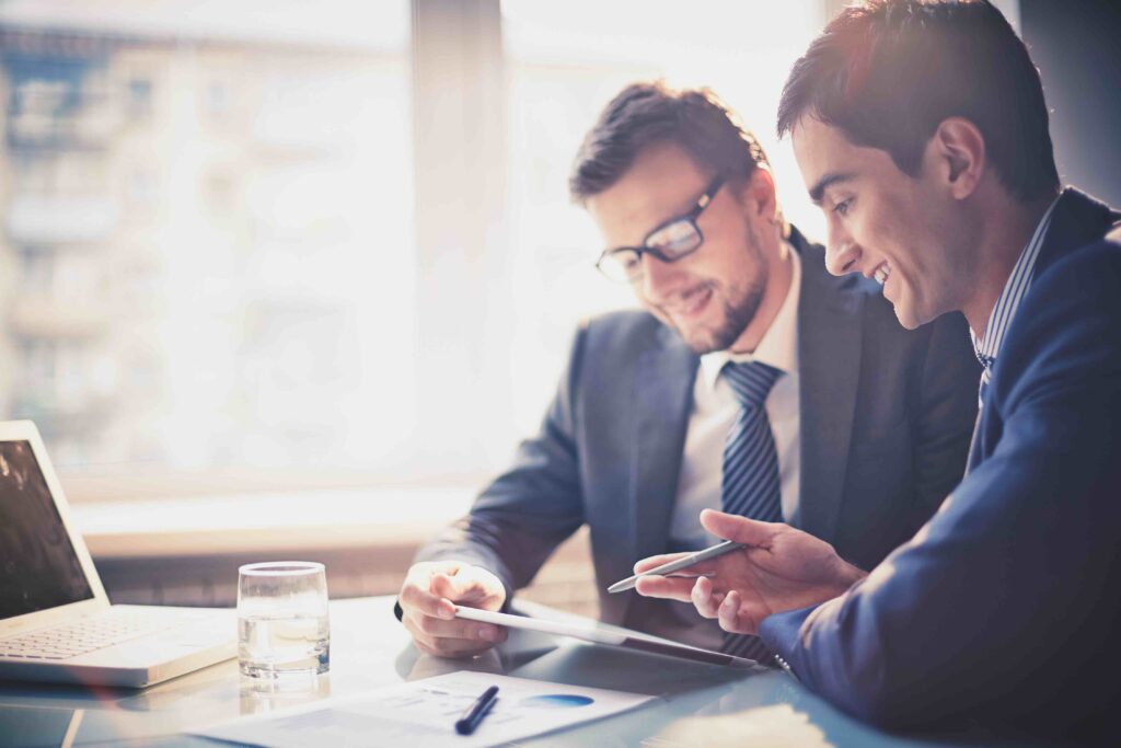 Two businessmen sitting at a table looking at a laptop.