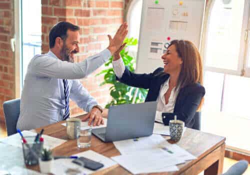 Two business people giving each other high fives in an office.