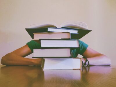 A person sitting at a table with a stack of books over their head.