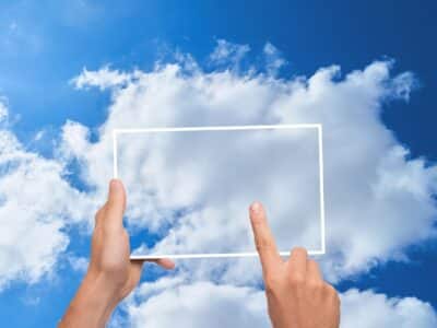 A hand is holding up a white frame against a blue sky with clouds.