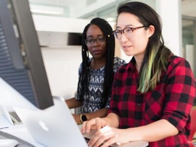 Two women working on a computer in an office.