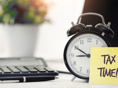 A yellow note with the word tax time on it sits on a desk next to an alarm clock.