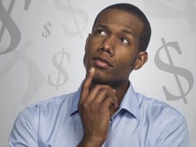 A man with his hand on his chin looking at dollar signs.