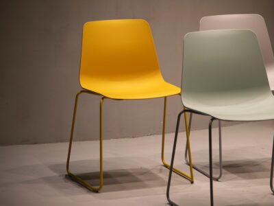 Three different colored plastic chairs in front of a gray wall.
