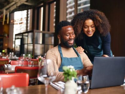 A man and woman using a laptop in a restaurant.