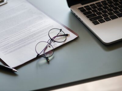 A laptop, glasses and a document on a desk.