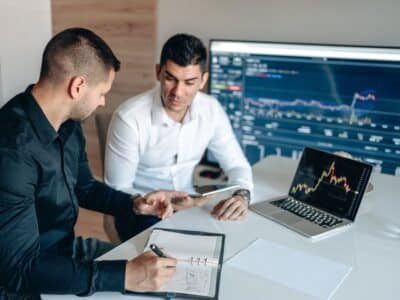 Two businessmen sitting at a desk and looking at a computer screen.