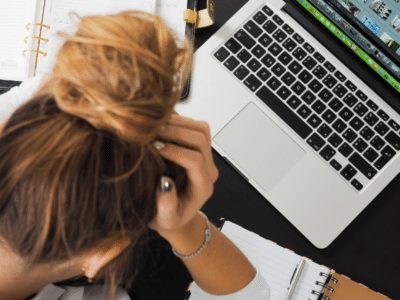 A woman is holding her head in front of a laptop.