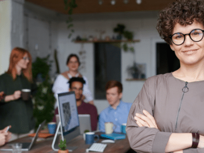 A woman in glasses standing in front of a group of people.