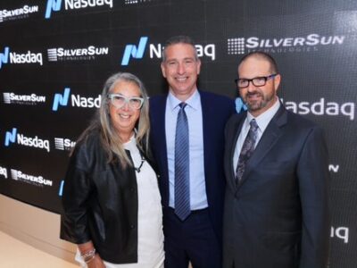 Three people posing for a picture in front of a nasdaq sign.