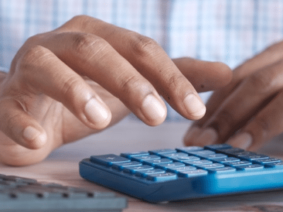 A man is using a calculator on a desk next to a cup of coffee.