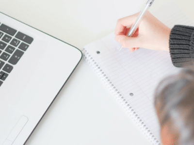 A person writing on a notebook next to a laptop.