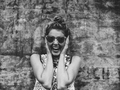 A black and white photo of a woman laughing in front of a wall.