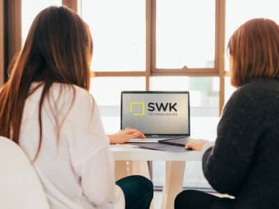 Two women sitting at a table with a laptop and SWK logo.