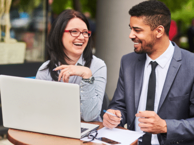 A man and woman sitting at a table with a laptop.