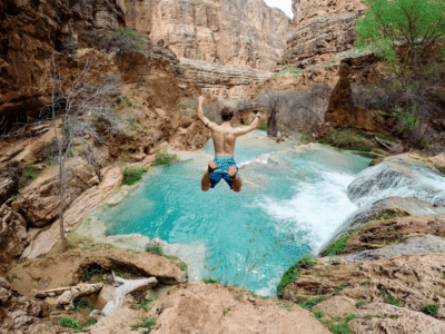 A man jumping into a river in a canyon.