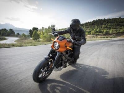 A person riding an orange motorcycle down a road.
