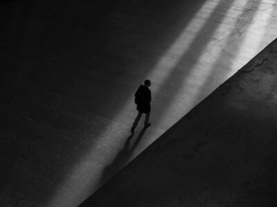 A black and white photo of a person walking in an empty room.