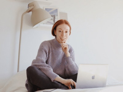 A woman sitting on a bed with a laptop.