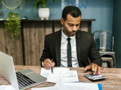 A man in a suit sitting at a desk and using a calculator.