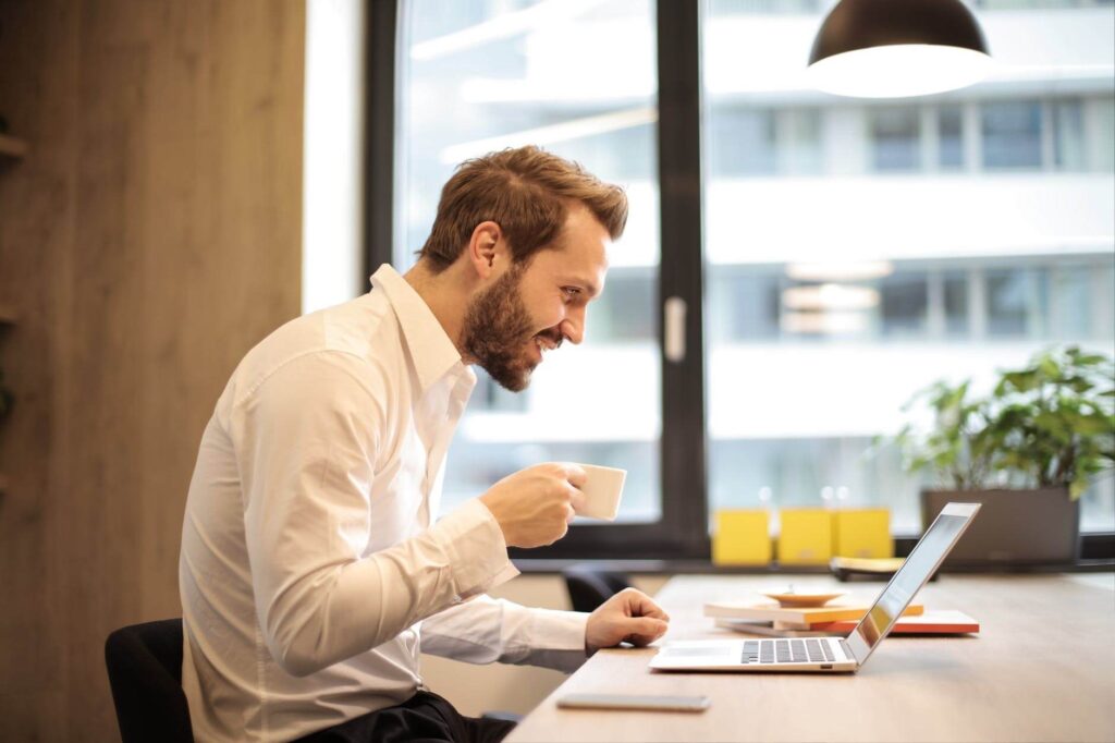 A man sitting at a desk with a laptop and a cup of coffee.