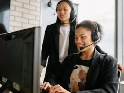 Two women in headsets working at a computer.