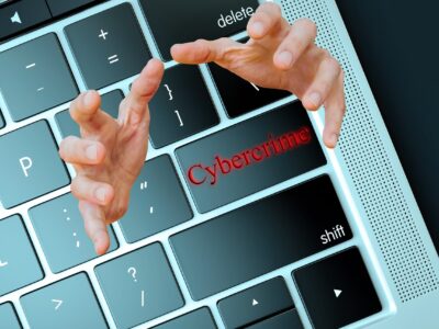 A person's hands are on a computer keyboard with the word cybercrime written on it.