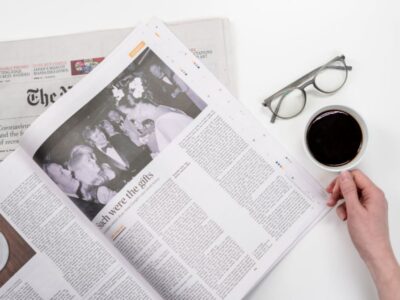 A woman is holding a newspaper and a cup of coffee.