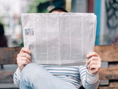 A man sitting on a bench reading a newspaper.