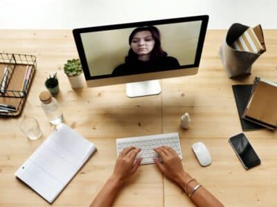A woman is working on a computer while a woman is on a video call.
