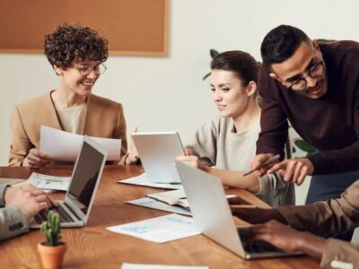 A group of people sitting around a table with laptops.