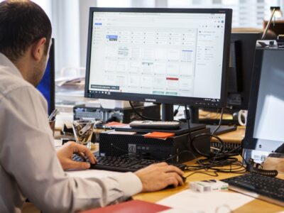 A man sitting at a desk with two monitors in front of him.