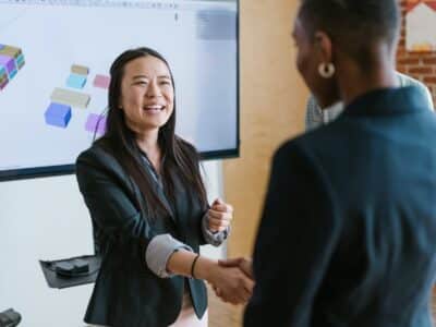 Two women shaking hands in front of a screen.